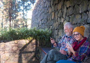 Fototapeta premium Two senior people resting on a sheltered bench after the hike in the mountains. Background of stones and forest. They check the cell phone