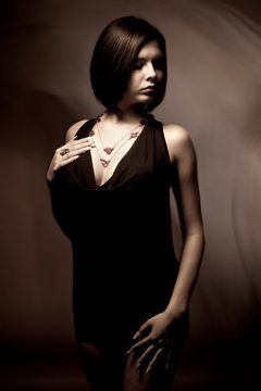 Monochrome portrait of the riddler beautiful slender girl in a black dress on a black background in the studio. Concept of femininity and beauty and grooming. Place for advertising