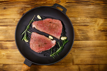 Raw pork steaks ready for preparation with rosemary, garlic and spices in cast iron grill frying...