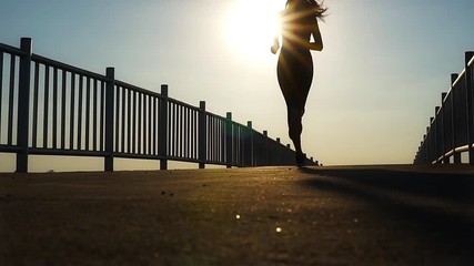 silhouette of fit woman jogging workout across the bridge while marathon practicing at the sunset