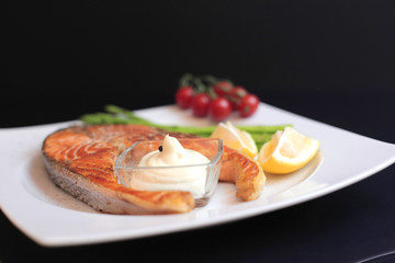 salmon steaks with vegetables and spices: asparagus, tomatoes, ginger, pepper corns, salt, chili, onion, lemon and olive oil on black background. Healthy food diet concept. Top view.