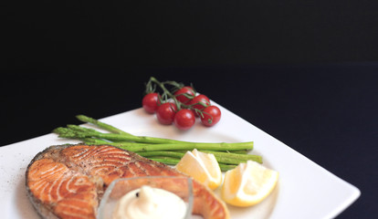 salmon steaks with vegetables and spices: asparagus, tomatoes, ginger, pepper corns, salt, chili, onion, lemon and olive oil on black background. Healthy food diet concept. Top view.