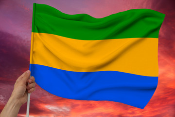 hand holds against the background of the sky with clouds the color flag of Gabon on the texture of...
