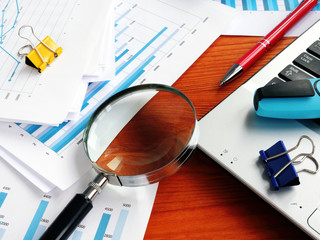 Internal business audit. Magnifying glass on the pile of financial reports.