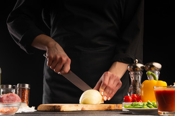 Chef cuts onions for cooking. On a black background. Cooking and Recipe Book. Delicious and wholesome food.
