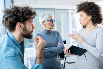 A manager and two employees discussing business in an office. The female employee is holding a notebook.