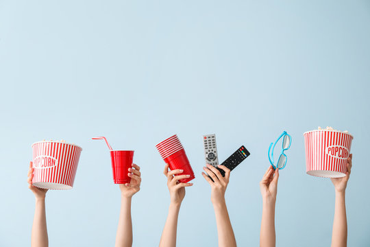 Many hands with popcorn, drink, remote controls and eyeglasses on color background