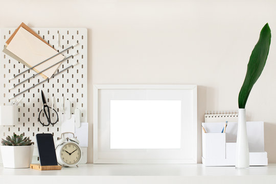 White home office desk with photo frame, supplies, flower. Minimal blank frame mockup design.