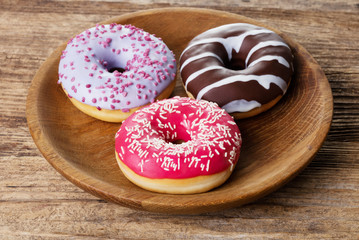 three various glazed doughnuts in plate on wooden background