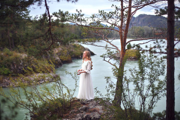  A girl in a white dress walks on a rocky shore near the river.