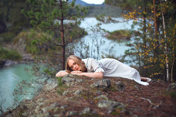  A girl in a white dress walks on a rocky shore near the river.