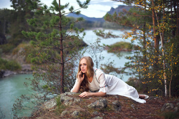 A girl in a white dress walks on a rocky shore near the river.