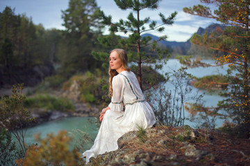  A girl in a white dress walks on a rocky shore near the river.