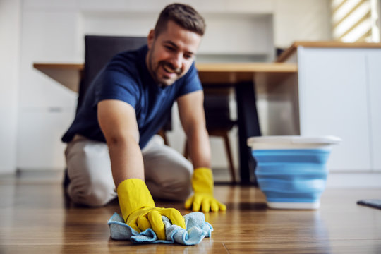 Man waxing parquet at home. Selective focus on hand with cloth. Rubber gloves on hands. Home interior.