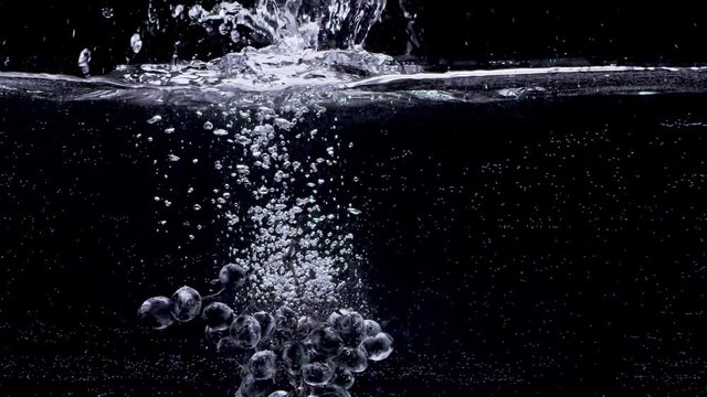 Bunch of grapes falling into water in slow motion. Isolated on black background. Close up view. Shot with cinema camera RED Dragon, UHD, 240fps.