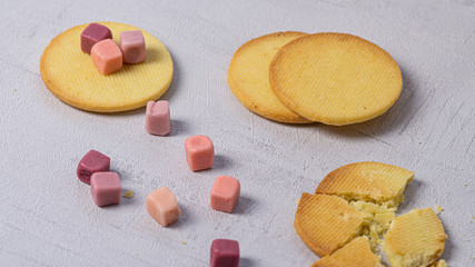 Few cookies on a table, one is crashed. There is some candies on a table and child hand putting down a candy on a cookie. 