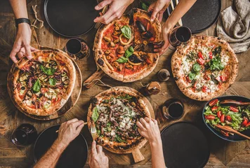 Foto op Aluminium Familie of vrienden die een pizzafeestje hebben. Plat leggen van mensen die verschillende soorten pizza& 39 s nemen en eten en rode wijn drinken over rustieke houten tafel, bovenaanzicht. Fastfood lunch, feest © sonyakamoz