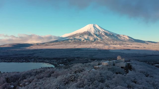 Aerial view of Mount Fuji in winter, iconic snow-capped symbol of Japan, snow covered scenery with freezing fog on trees, lake Yamanaka, clear blue sky - landscape panorama of Japan from above, Asia