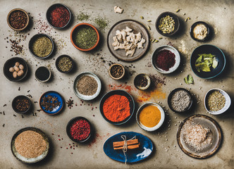 Obraz na płótnie Canvas Flat-lay of spices in bowls and plates over grey background, top view. Black pepper, allspice, cloves, thyme, cumin, sesame, star anise, ginger, cinnamon, cardamom, mahlep, smoked salt, rosemary, bay