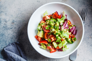 Avocado and tomato salad in white bowl, top view. Vegan food concept.
