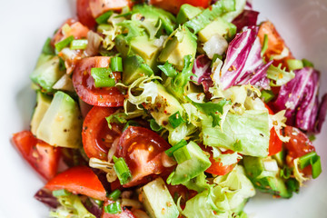 Avocado and tomato salad in white bowl. Vegan food concept.