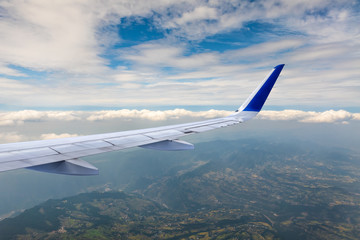 Fototapeta premium Airplane flying at high altitude over green mountains and sky at sunrise