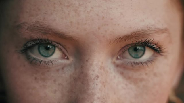Close up video of Woman’s green Beautiful Eyes looking at Camera Objective. Opening her Eyes Slowly and having Confident look. Girl with natural beauty and freckles on her Charming face