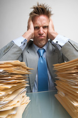 Frustrated office worker frowning at the large stacks of file folders on his desk