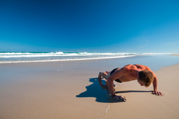 Unrecognizable man doing pushups outdoors on wide empty beach