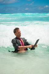Fototapeta premium Cheerful castaway businessman using a tablet computer in tropical waves