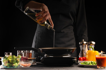 Cooking, the chef pours oil in a pan, against the background of vegetables. Cooking. Recipe book, cooking and gastronomy.