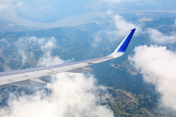 Airplane flying at high altitude over green mountains and sky at sunrise