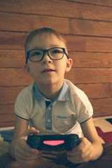 Caucasian boy in glasses sitting in his room on the bed with a joystick in his hands. he plays...