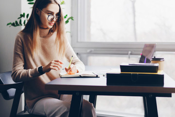 Female executive sitting at desk in office, using portable digital devices for work. Girl typing on laptop and texting on smartphone. Young woman taking selfie at workplace