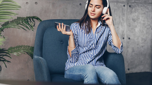 Girl listening to music in earphones. Young woman downloading favorite songs on her smartphone. Audio apps with great entertainment content for mobile phone users.