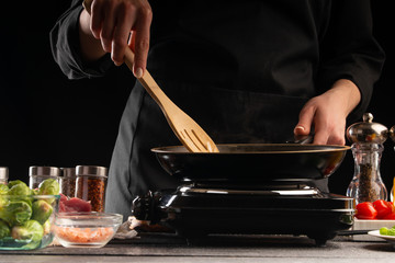 Chef cook fried in a pan against the background of fresh vegetables, culinary recipes