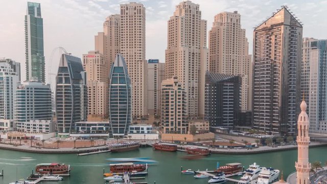 Yachts in Dubai Marina flanked by the Al Rahim Mosque and residential towers and skyscrapers aerial timelapse. Modern high rise skyline with boats and wooden dhows