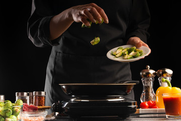 Cooking, the chef fries the Brussels sprouts in a pan, against the background of vegetables. Freezing in motion. Cooking. Recipe book, cooking and gastronomy.