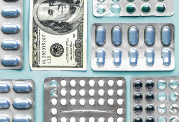 white and blue pills in blister with money dollar on a blue background, medicine flat lay