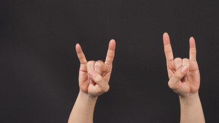 Male model is doing rock hand sign with two hands on blackground.