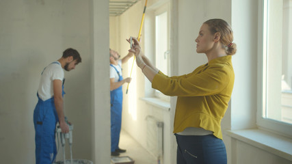Woman makes a photo on phone, repairmen work in the flat