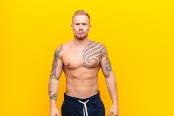 young strong blonde man looking goofy and funny with a silly cross-eyed expression, joking and...