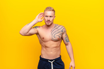 young strong blonde man looking serious and curious, listening, trying to hear a secret...