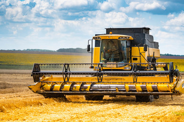 Fototapeta na wymiar A modern combine harvester with a large mower in a wheat field. Agricultural seasonal work.