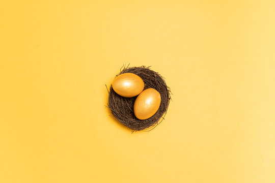 Top view of gold easter decor eggs in wicker nest on yellow background. Holiday composition card