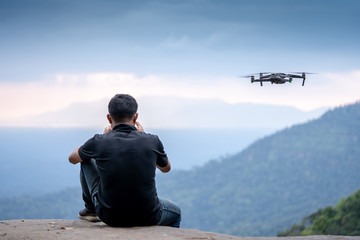 Man operating drone flying or hovering by remote control in the jungle.