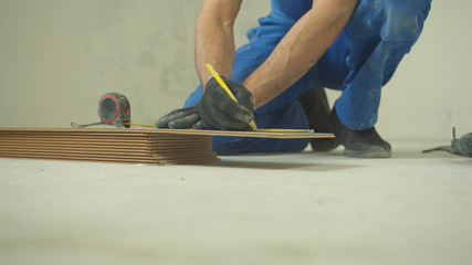 Repairman sits and measures a length of a tile