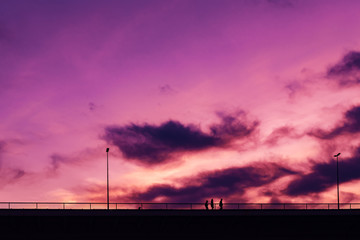 Silhouettes of three young people crossing the bridge in sunset