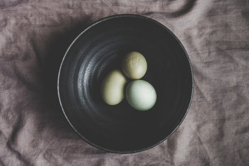 Obraz premium organic eggs in black ceramic bowl moody flat lay indoor photo