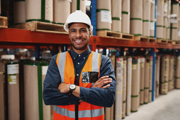 Confident african american man standing with folded arms in manufacturing unit with white helmet and uniform in factory